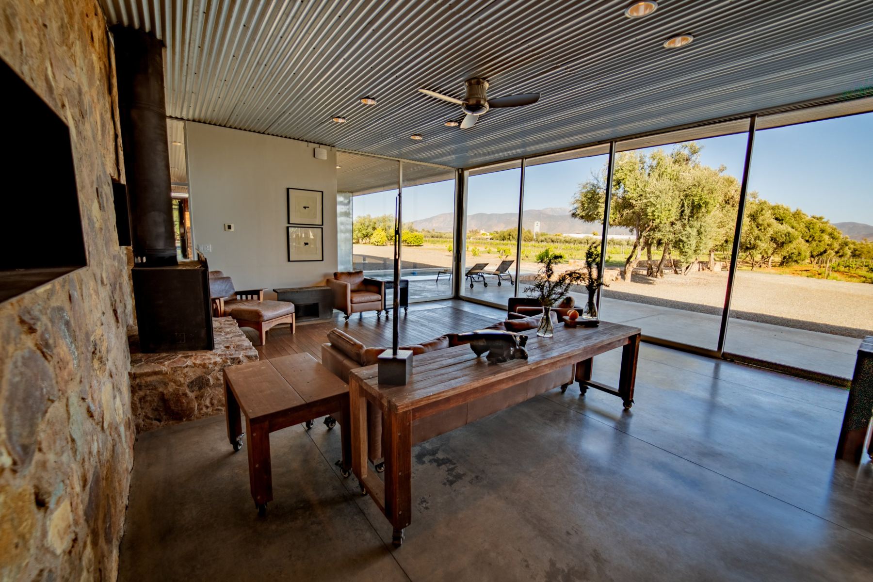 La sala principal con chimenea de piedra y ventanales hacia los olivos y las montañas