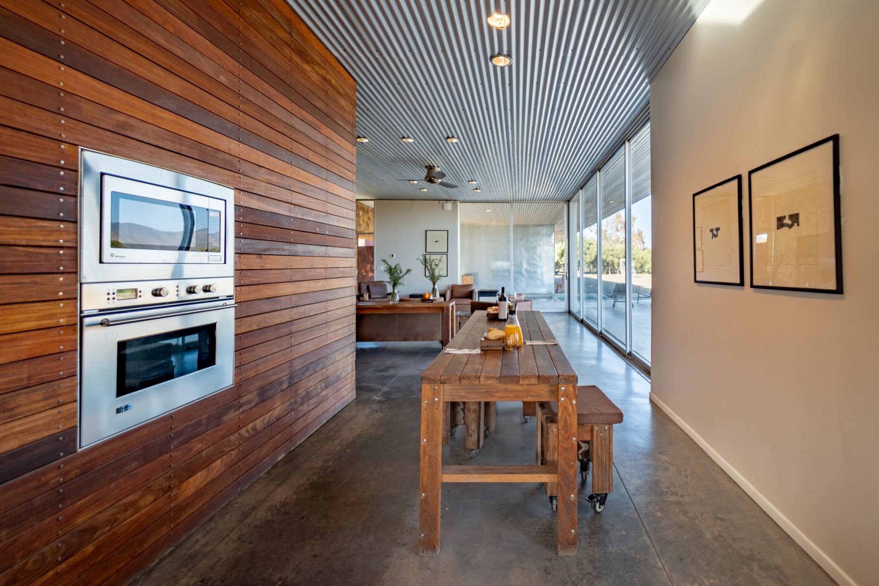 Muro de cocina en madera con hornos empotrados junto a una larga mesa